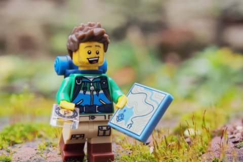 A lego toy character holds a compass and map.