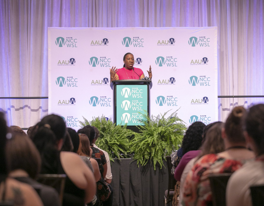A Black female speaker at a lectern in front of an AAUW audience.
