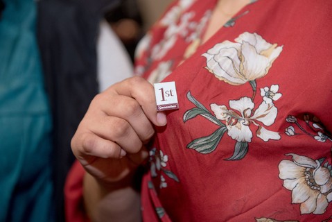 A woman in a blouse holds a button on her blouse that says first generation