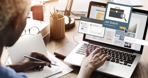 Person sitting at a desk with papers and laptop, perceived to be searching for a job