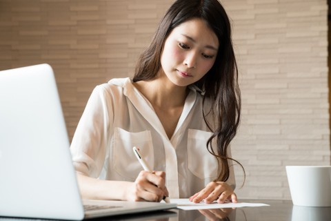 Image of female sitting at a desk with laptop and coffee, and taking notes.