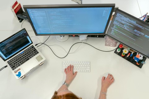 A woman at her desk with three monitors that are displaying code.