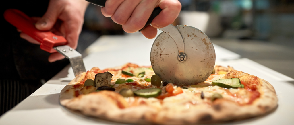 A close up of a pizza cutter as it slices through a hot freshly baked pizza