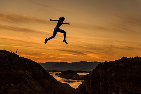 female runner jumping over a crevice at sunset