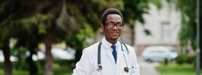 A person in a white coat stands in front of trees.