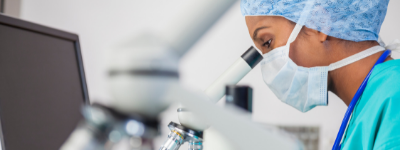 A person wearing a mask looks at a microscope.