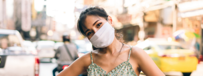 A friendly-looking woman wearing a mask in a city.