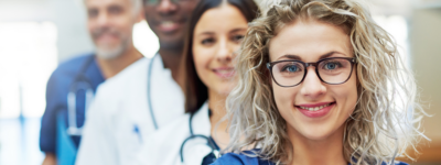 A woman wearing glasses and wearing scrubs smiles at the camera.