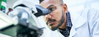 A man wearing a lab coat looks into a microscope.