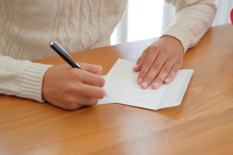 person in white sweater with only hands visible writing a letter with a pen and paper