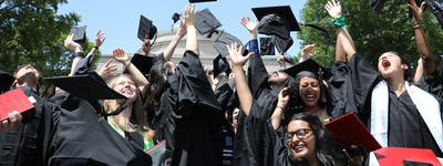 a group of newly graduated MIT alum in caps and gowns, celebrating and throwing their caps in the air