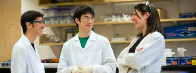 Three people in white lab coats laugh together.