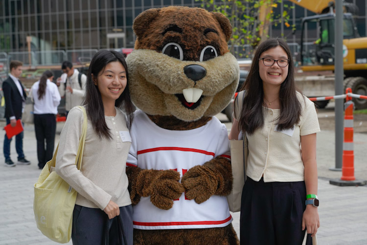 Two students standing smiling with Tim the MIT mascot at the fall career fair-fcf