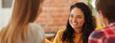 A smiling woman speaks to two other people in a casual setting.