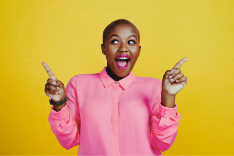 A person wearing a bright pink shirt smiles broadly in front of a plain yellow background.