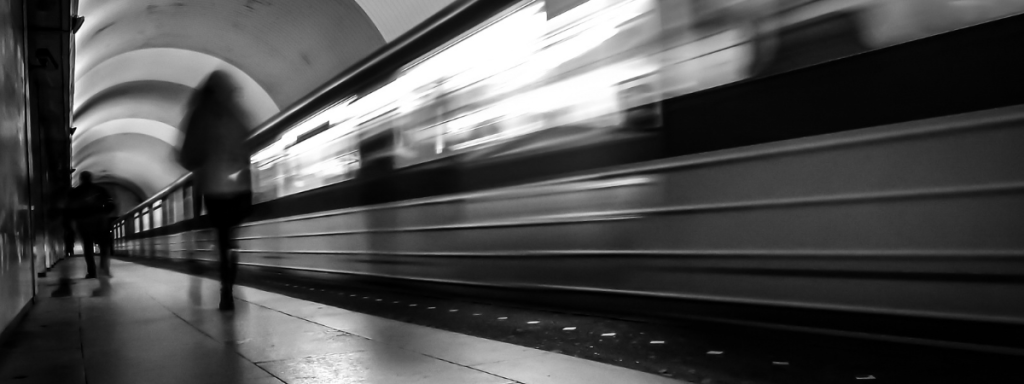 A person walks past a moving, motion-blurred subway train.