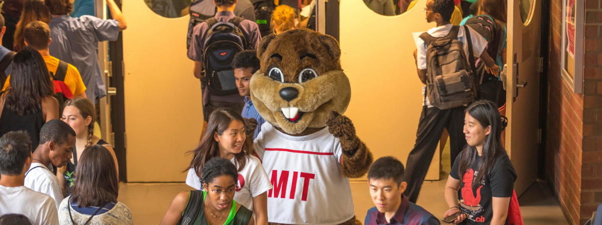 Tim the Beaver waves at MIT students in a hallway.