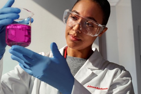 A lab researcher holds and looks at a glass beaker full of purple liquid