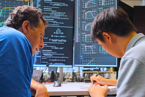 two men working closely with figures on a screen behind them