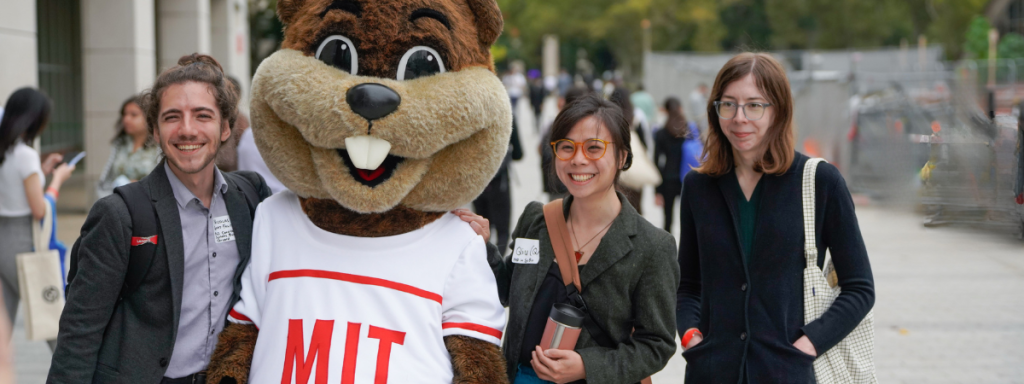 Recruiting fair scene with MIT's Tim the beaver and three smiling students