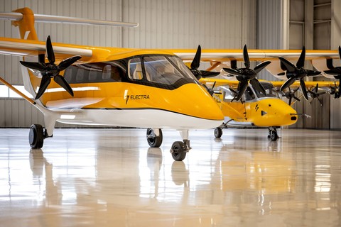 Two yellow-and-white electric aircraft with black propellers parked inside a bright aircraft hangar, with one aircraft prominently in the foreground and another behind it.