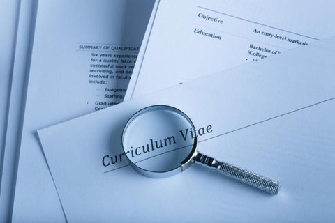 multiple resumes and cvs stacked with a magnifying glass rested on top