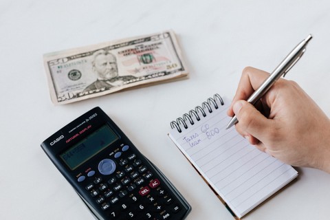 Financial planning with a calculator, money, and notebook with a hand writing notes.