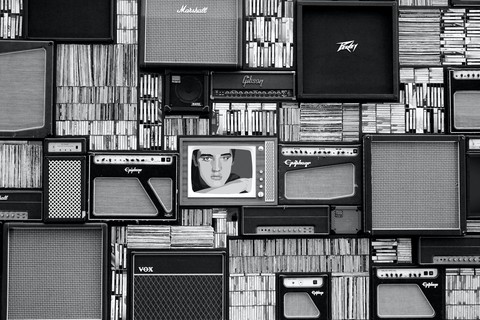 Plack and white photo of books stacked on speakers in the center is a television with a portrait of Elvis Presley
