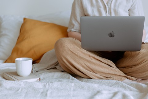Person sitting in bed with laptop on their lap and a coffee beside them