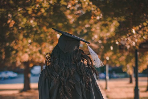 Student with a cap and gown walking down a sidewalk