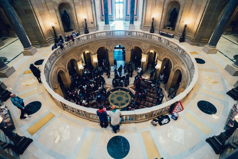 Inside a federal building a group of people are gathered in an inner circular structure with arched pillars on the main floor