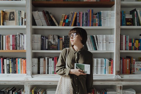 Person standing in front of bookshelf while holding a book
