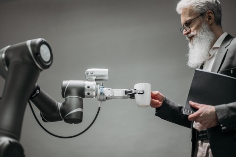 Robot hand and arm handing a coffee cup to a person holding a notebook