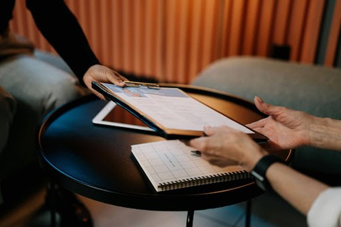 A person handing a resume on a clipboard over a circular table to a person on the other side.