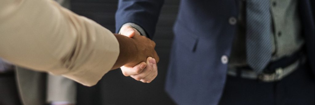 Person in business attire shakes hand of someone else in a blazer