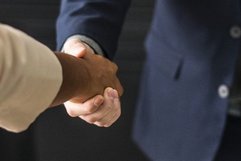Person in business attire shakes hand of someone else in a blazer