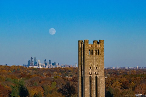A full moon rises over the Philadelphia skyline and Swarthmore College's Clothier Bell Tower in November 2025. Between the Philly skyline and Bell Tower is fall foliage.