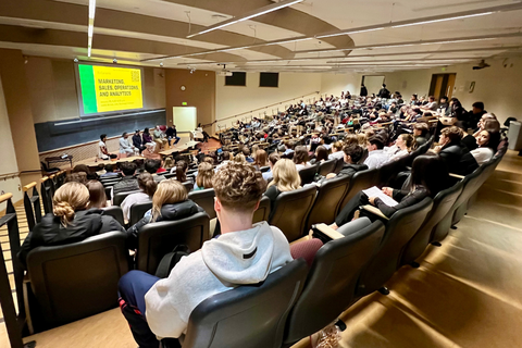 Students gather in an auditorium-style lecture hall to watch panelists presenting on career paths in marketing, sales, operations, and analytics.