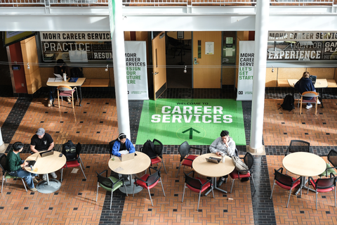 Overhead view of Mohr Career Services office from the atrium balcony. Round tables with students studying are in the foreground, and the words