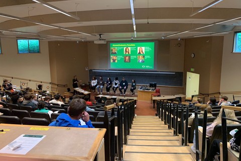 Lecture hall during a BizCareers event with students seated and watching a panel of speakers beneath a projected slide introducing alumni and industry panelists.