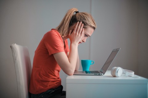 Young woman gazing at laptop with her hands on her head
