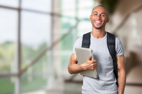 Young black college student holding a laptop and wearing a backpack.