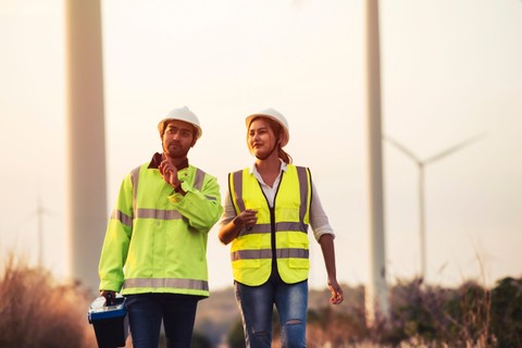 Young Asian maintenance engineers team working in wind turbine farm at sunset.