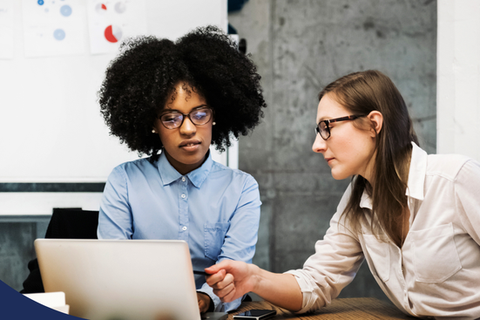 a young person consulting with a colleague near a laptop.