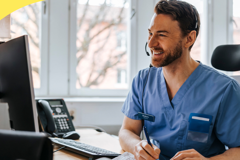 Person in scrubs wearing a headset at a computer.