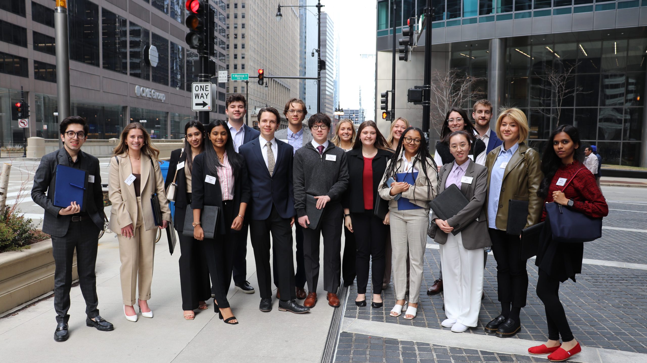 A group of 17 students stand in 2 rows on a sidewalk. They are the participants of the 2023 Career Trek in Chicago.