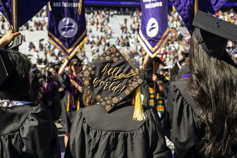 Student at graduation ceremony facing away from camera wearing a cap decorated with gold flowers and cursive inscription 