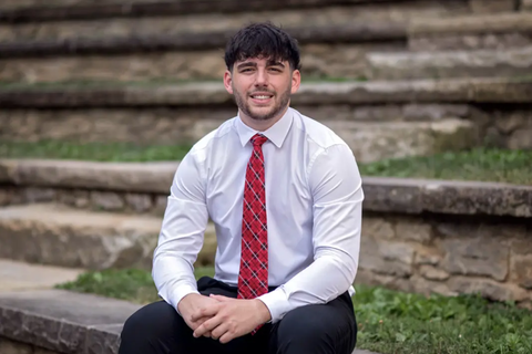 A young man in a white button down shirt with a red tie sitting on a set of stone steps.