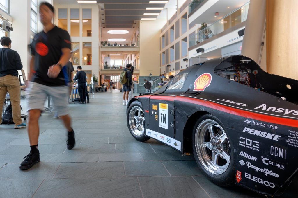 Students walk through Duffield Hall past an engineering project team car.