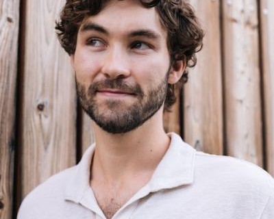 Man with facial hair in front of a wooden fence, looking upwards